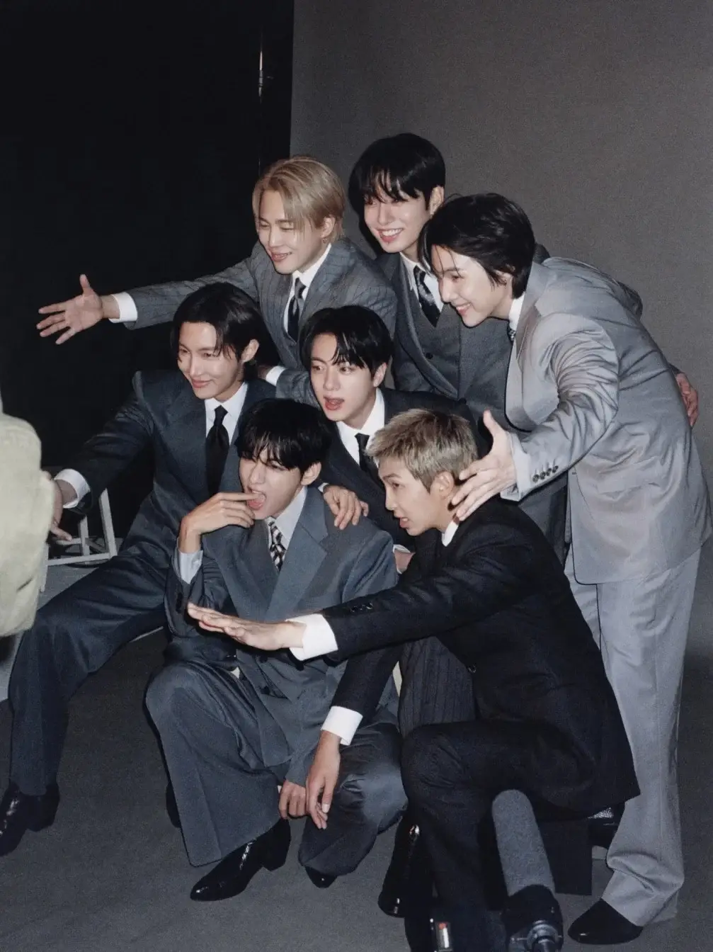 A high-energy group shot of all seven BTS members posing together in stylish outfits.