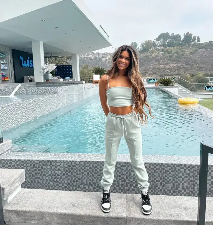 Taylor Frankie Paul smiling in a light green crop top and sweatpants set by a luxury infinity pool with mountain views.