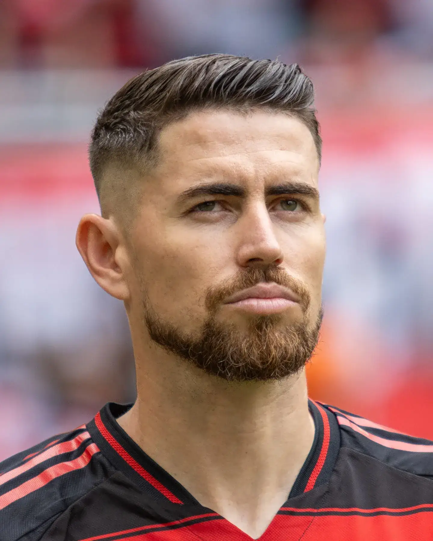 A focused headshot of Jorginho looking off-camera while wearing a black and red Arsenal training kit.