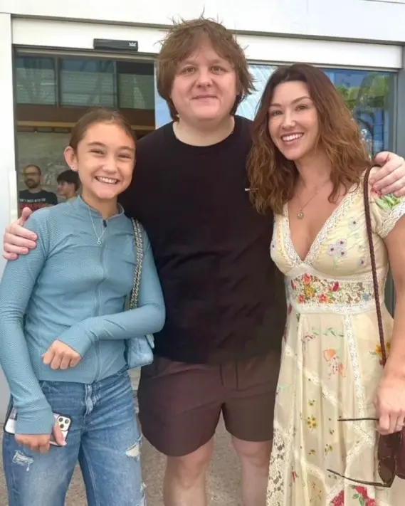 Jude Law’s daughter Iris Law smiles alongside Lewis Capaldi and a friend in a casual outdoor setting.