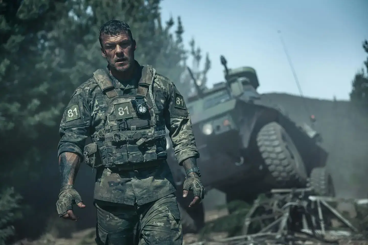 Alan Ritchson walks through a smoke-filled forest wearing military
