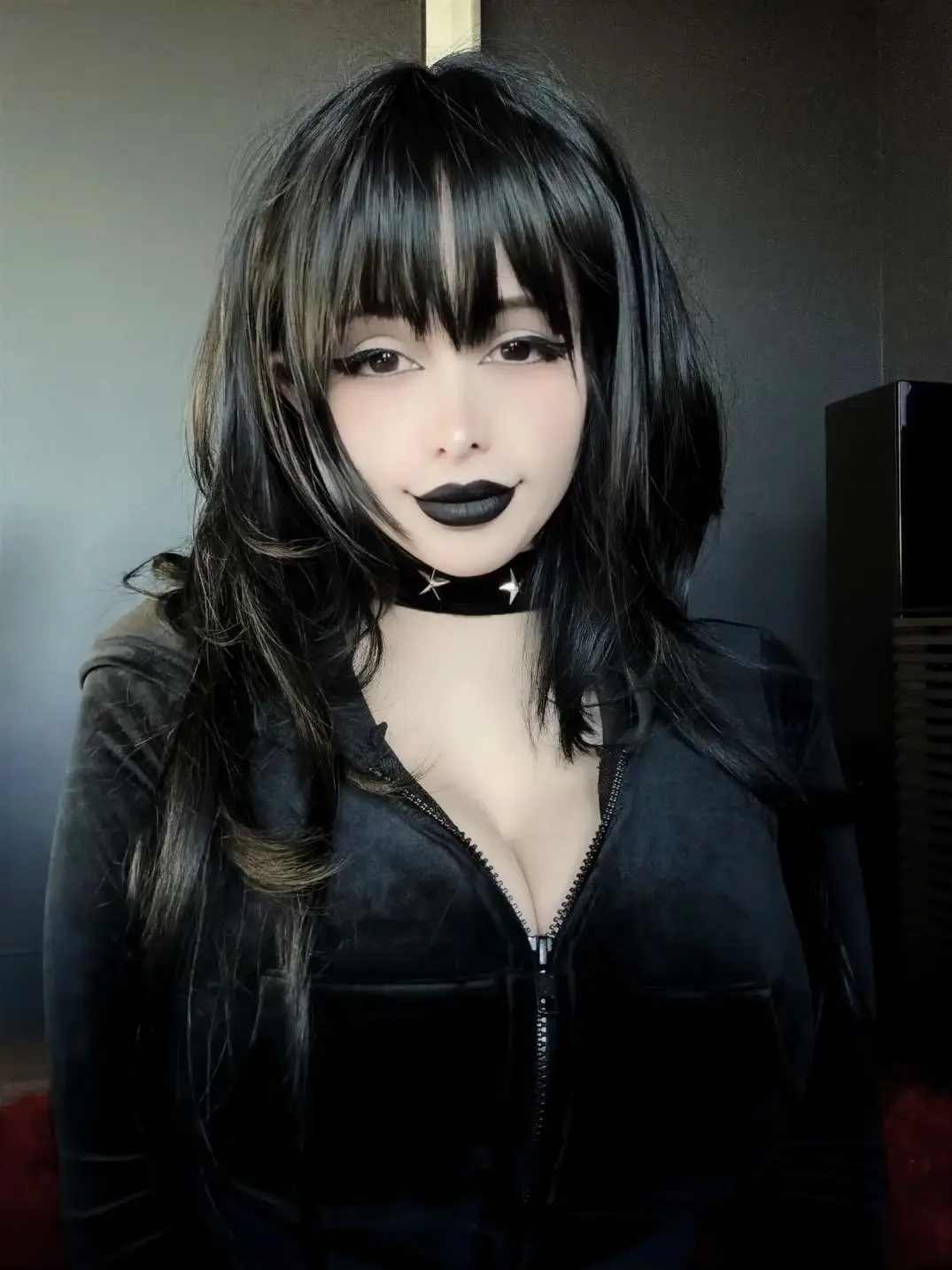 Pinkchyu poses with long black hair, gothic makeup, and a black velvet zip-up top.
