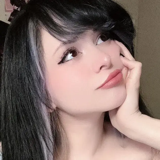 Pinkchyu looking upward with her hand on her cheek, showcasing her black hair with purple highlights.