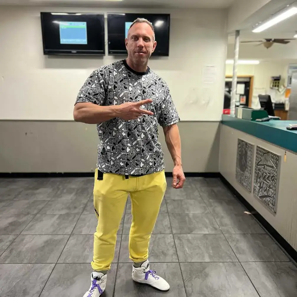 ectone stands in a tiled room wearing a patterned t-shirt, bright yellow sweatpants.