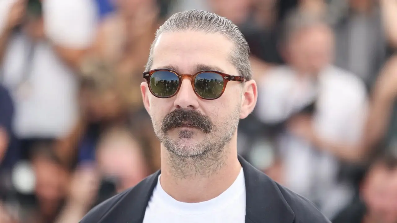 hia LaBeouf sporting a mustache and tortoiseshell sunglasses at a red carpet event.