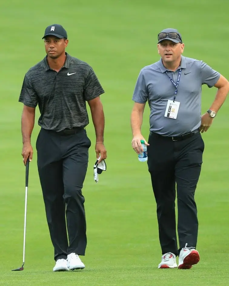 Tiger Woods and Rob McNamara walking together on a green golf course during a tournament.