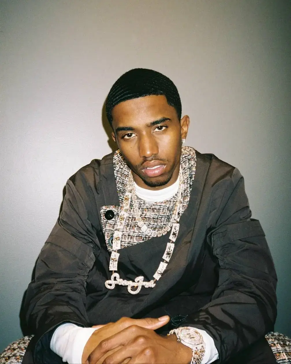 Christian Combs’ posing in a layered jacket and Sean John diamond chain against a gray backdrop.