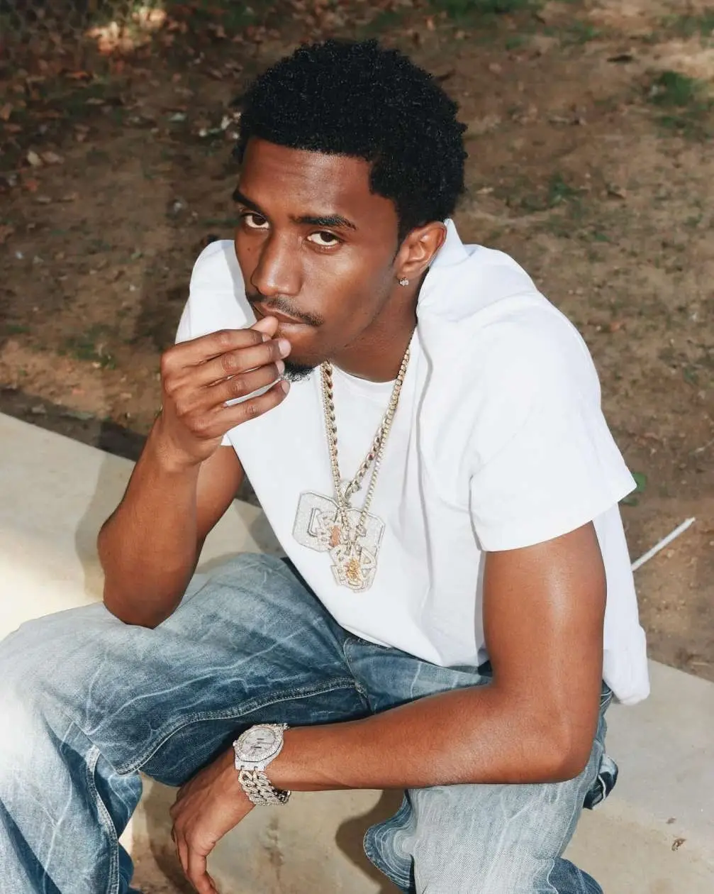 Christian Combs’ sitting outdoors in a white t-shirt and jeans, wearing a diamond watch and necklaces.