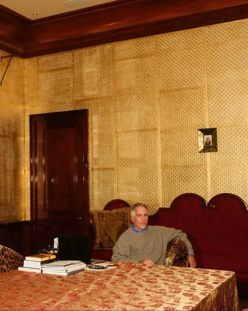 Jeffrey Epstein sitting on a red velvet sofa in a room.