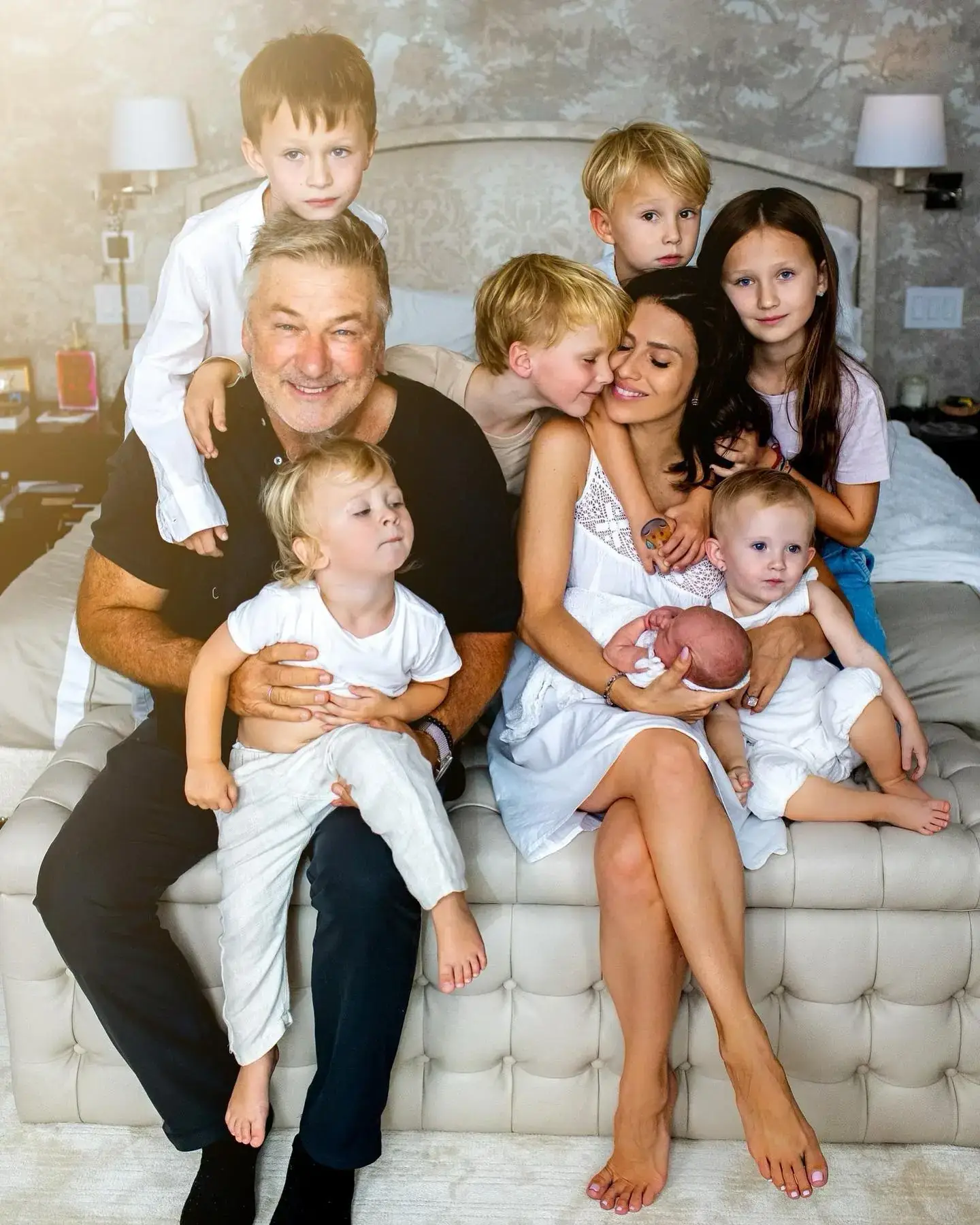 Alec Baldwin and Hilaria Baldwin’s family posing for a crowded, affectionate group portrait on a tufted bench with their seven children.