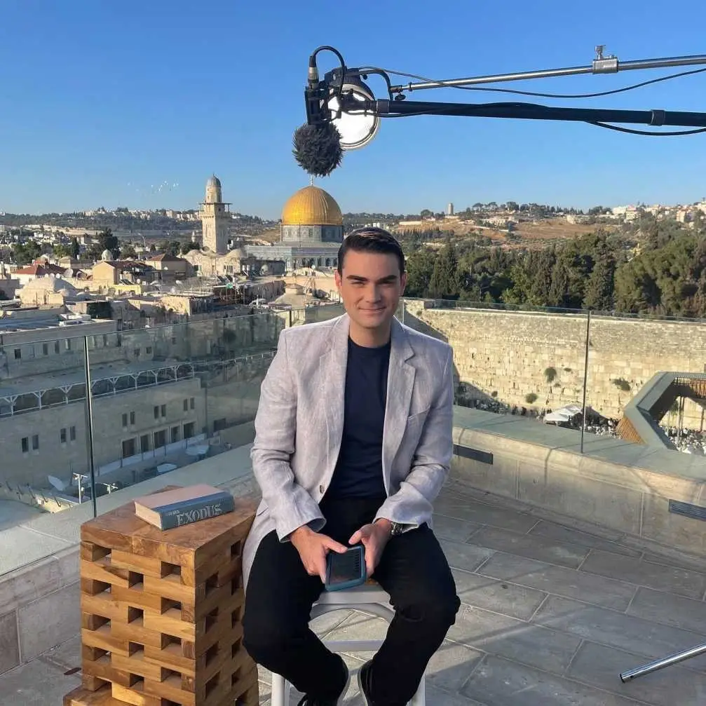 Ben Shapiro sitting on a rooftop in Jerusalem with the Dome of the Rock in the background.
