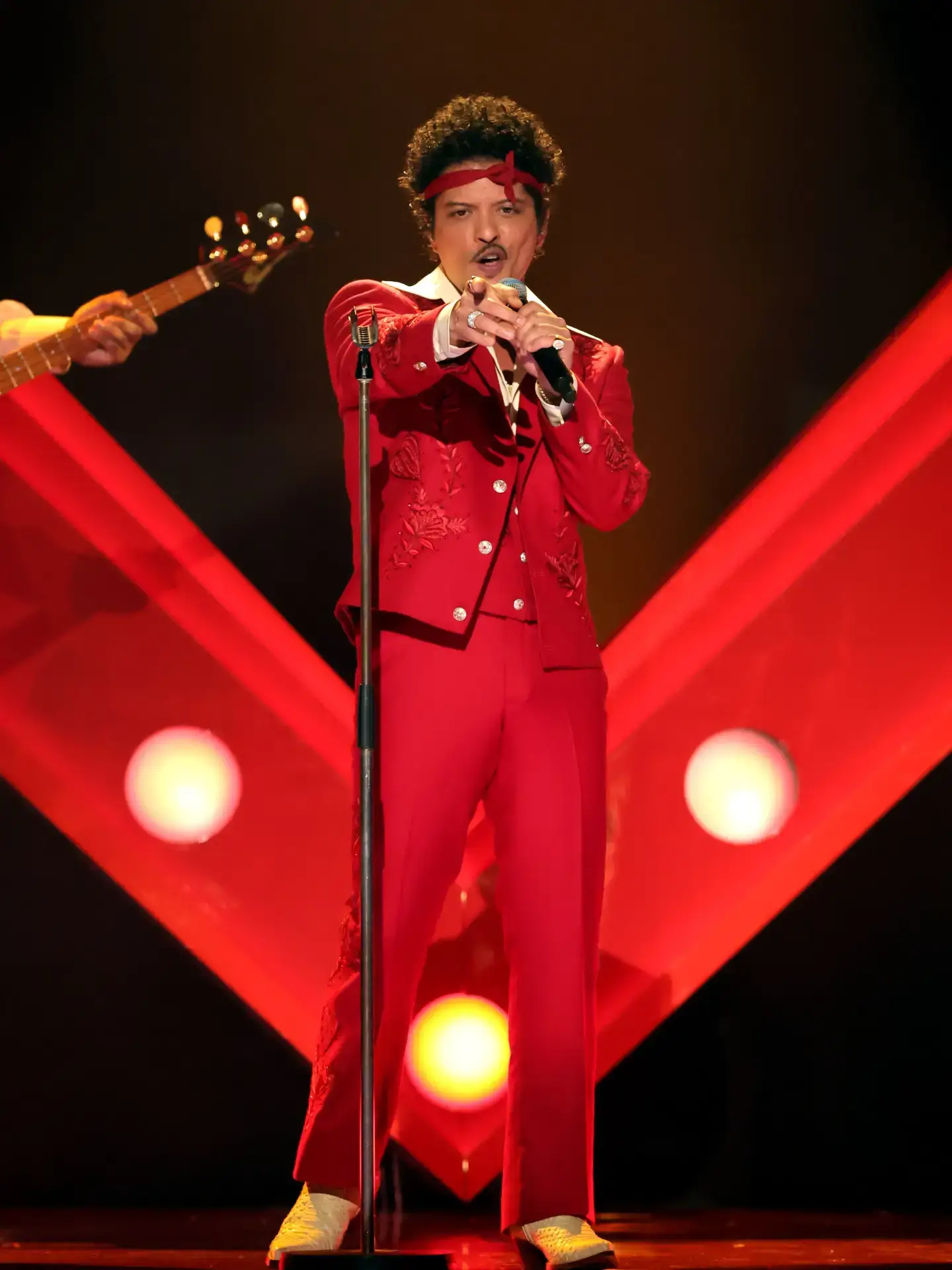 Bruno Mars performs on stage in a vibrant red suit and headband.