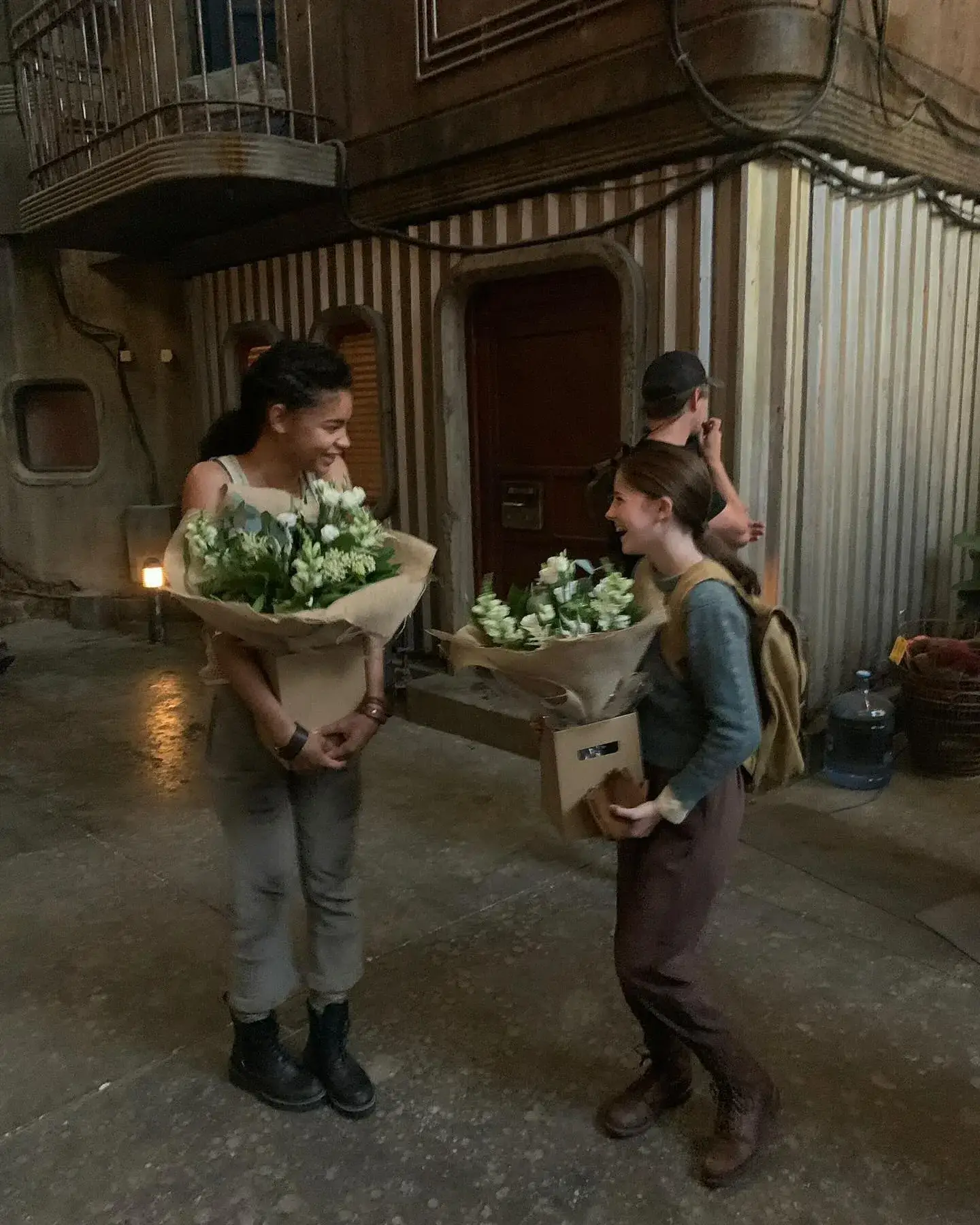 Ida Brooke and amelie.jsy smiling together while holding large bouquets of white flowers on a rustic film set.