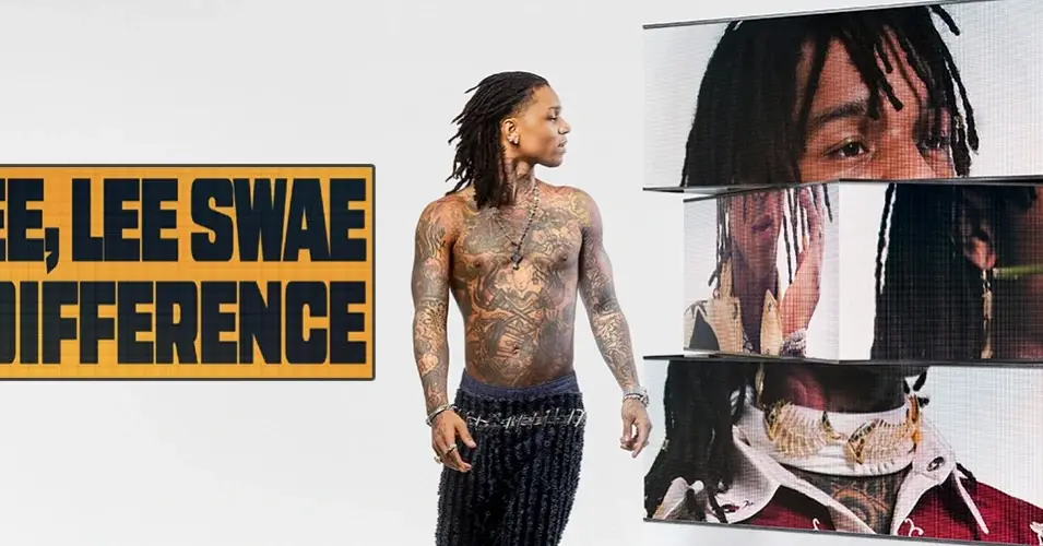 Rapper Swae Lee stands shirtless showcasing his tattoos next to a digital display of his own portraits.