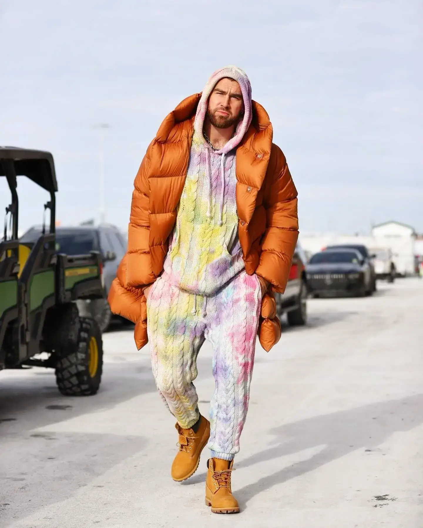 NFL star Travis Kelce walks outdoors wearing a vibrant tie-dye cable-knit tracksuit