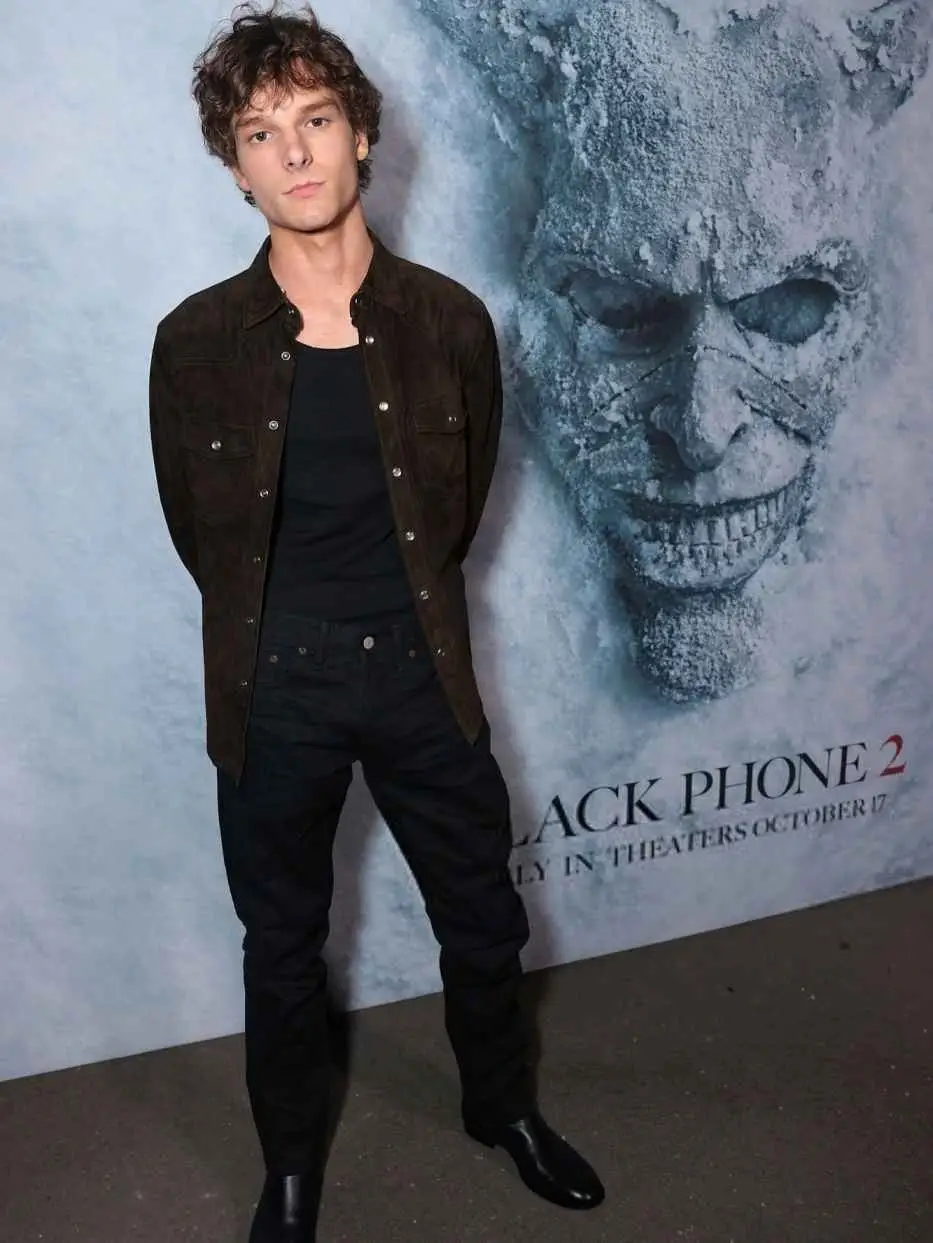 Mason Thames standing in front of a promotional poster for the horror film The Black Phone 2.