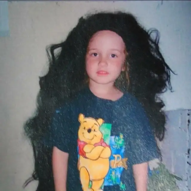 A young Cailee Spaeny wearing an oversized, voluminous black wig and a Winnie the Pooh t-shirt.
