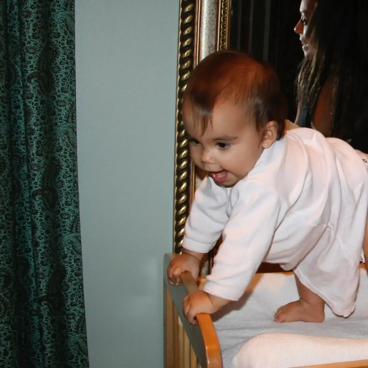 A candid childhood photo of Ariana Greenblatt as a baby, smiling while playfully standing in her crib.