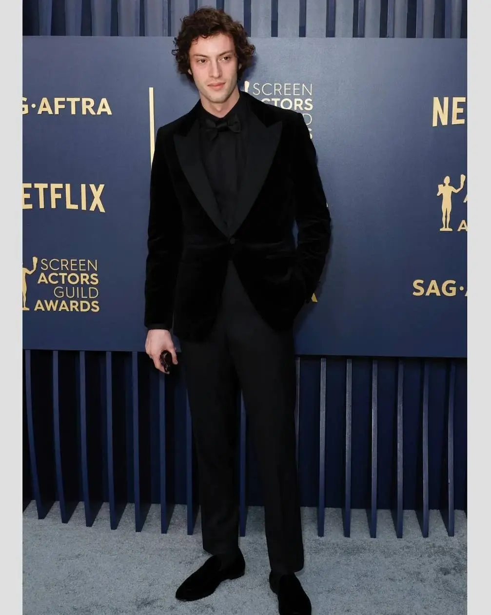 Dominic Sessa posing on the Screen Actors Guild Awards red carpet wearing a black velvet tuxedo.
