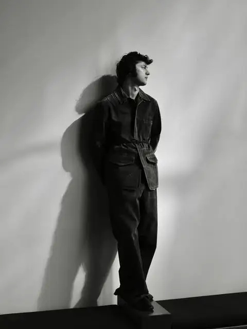A black and white photo of Dominic Sessa’s profile as he leans against a wall in a denim utility suit.