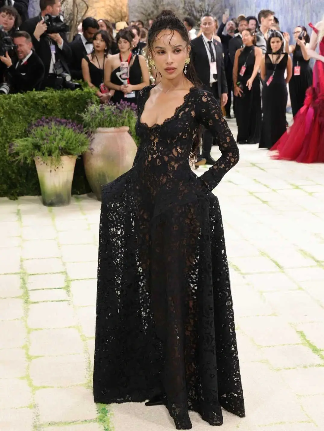 Jessica McCormack poses on a red carpet in a long-sleeved black lace gown with her hands tucked into sculptural pockets.