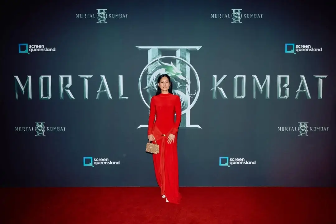 Ana Thu Nguyen stands on a red carpet in a long red dress in front of a Mortal Kombat 2 backdrop.