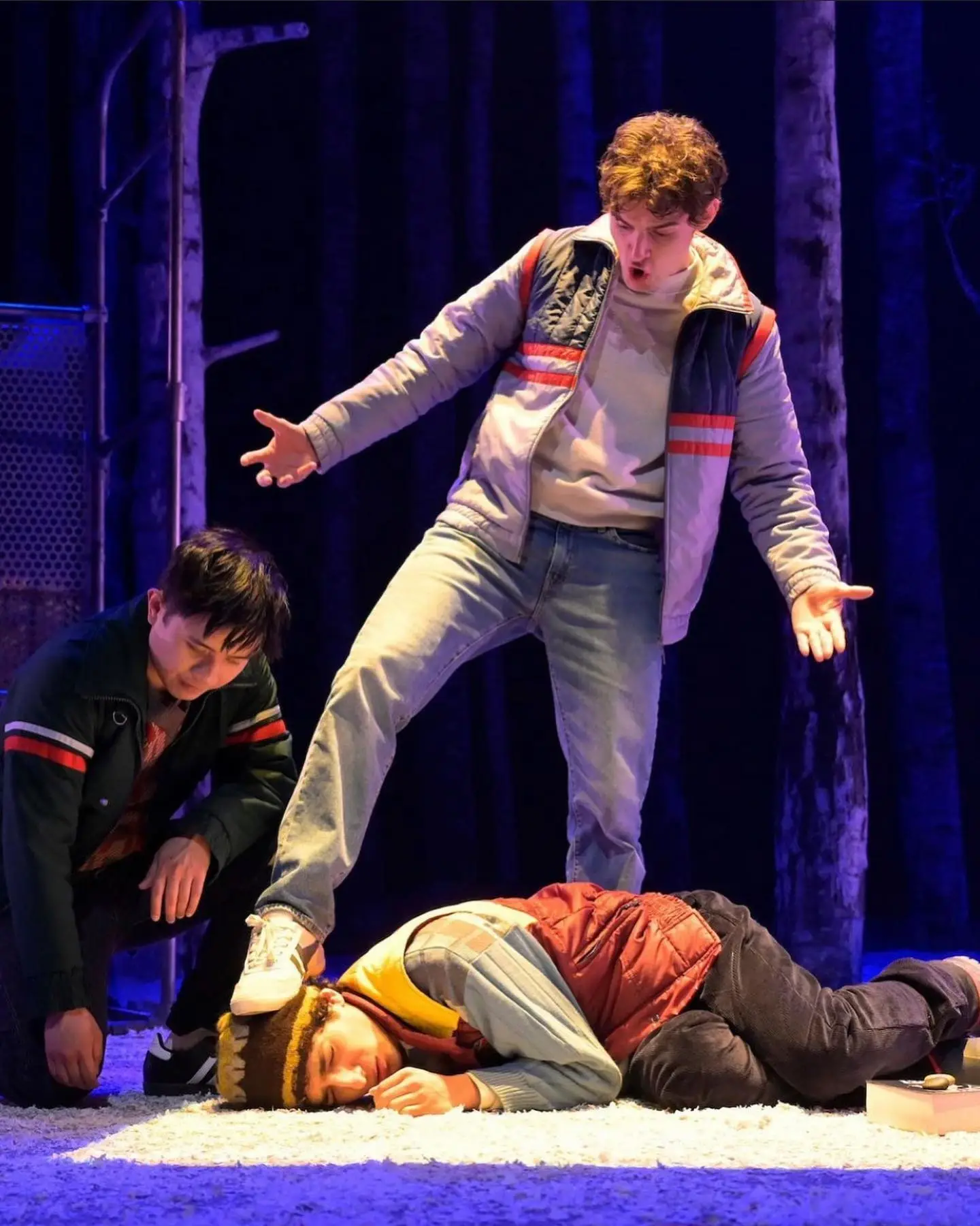 Michael Johnston performs a dramatic scene on a theater stage, standing over a fallen character in a wooded set.