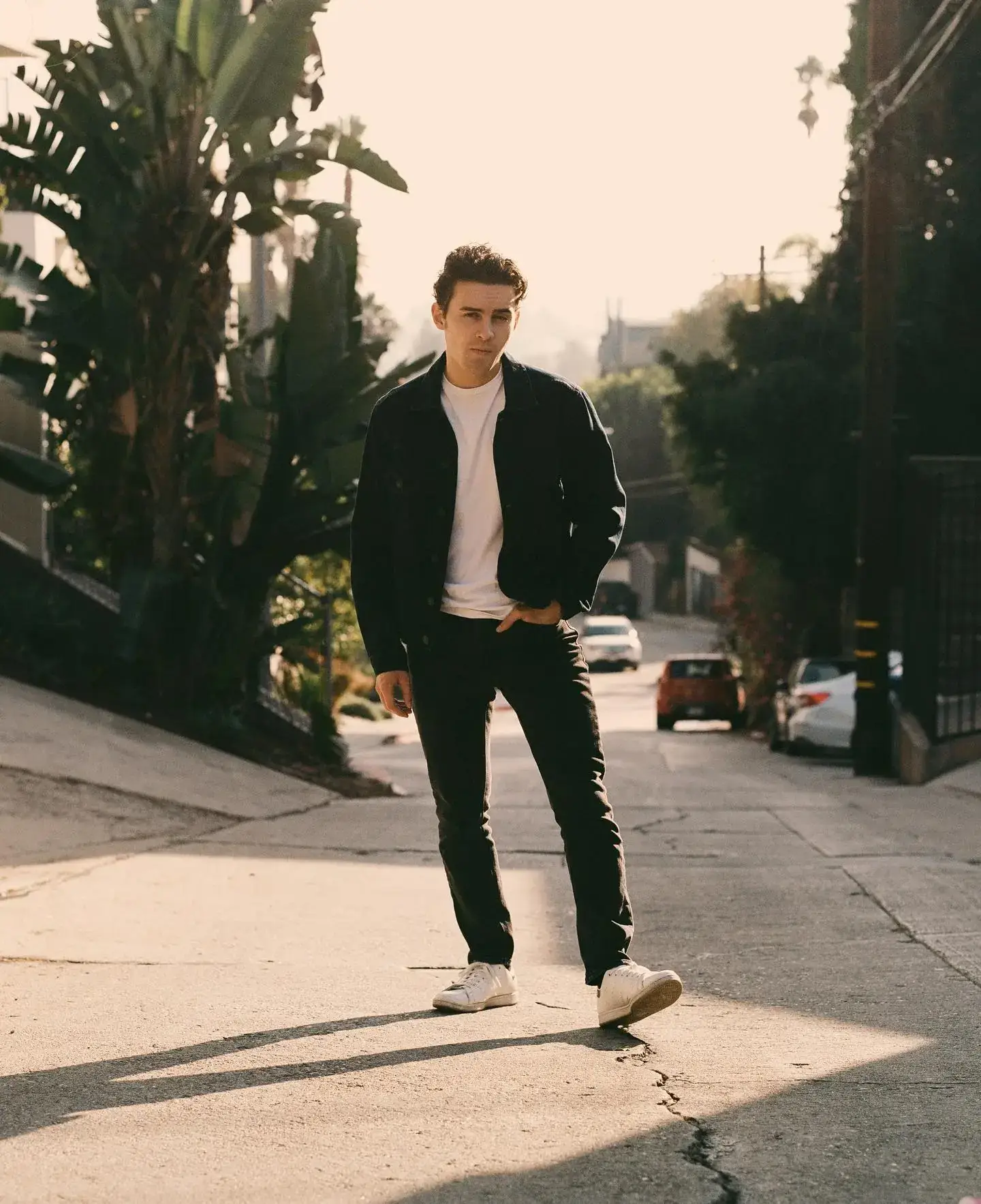 Michael Johnston poses in a black denim jacket and white t-shirt on a sun-drenched street.