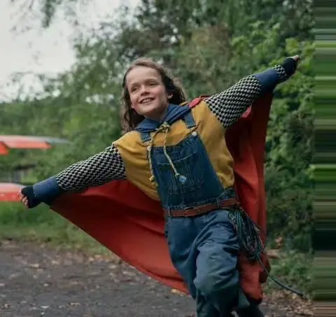 A joyful young boy with long hair runs through a wooded area.