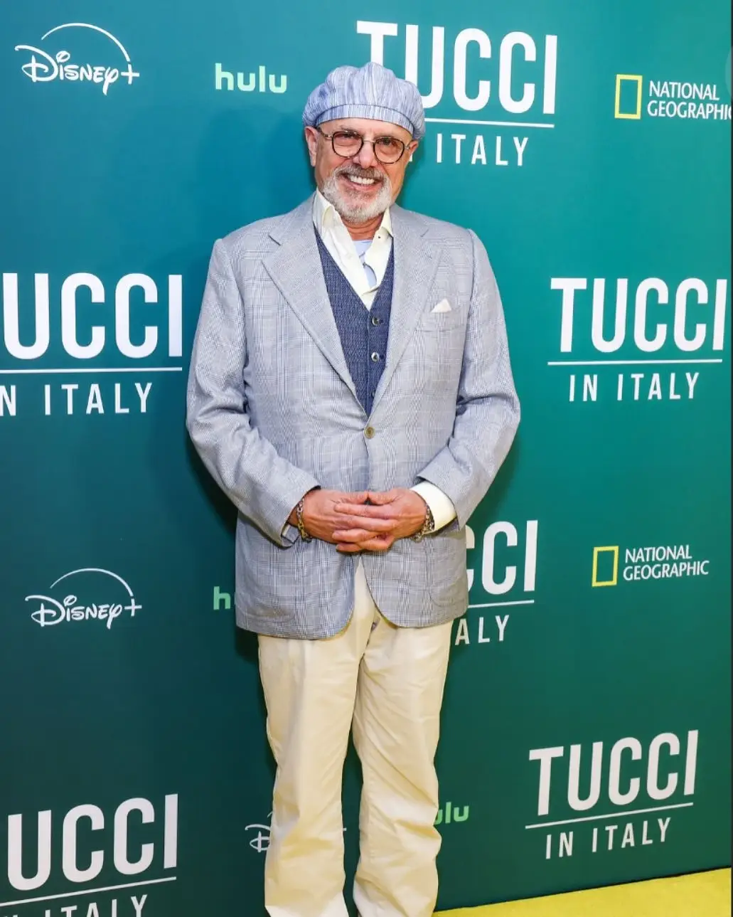 Joe Pantoliano poses on a green carpet in a light blue patterned blazer, matching flat cap, and beige trousers.