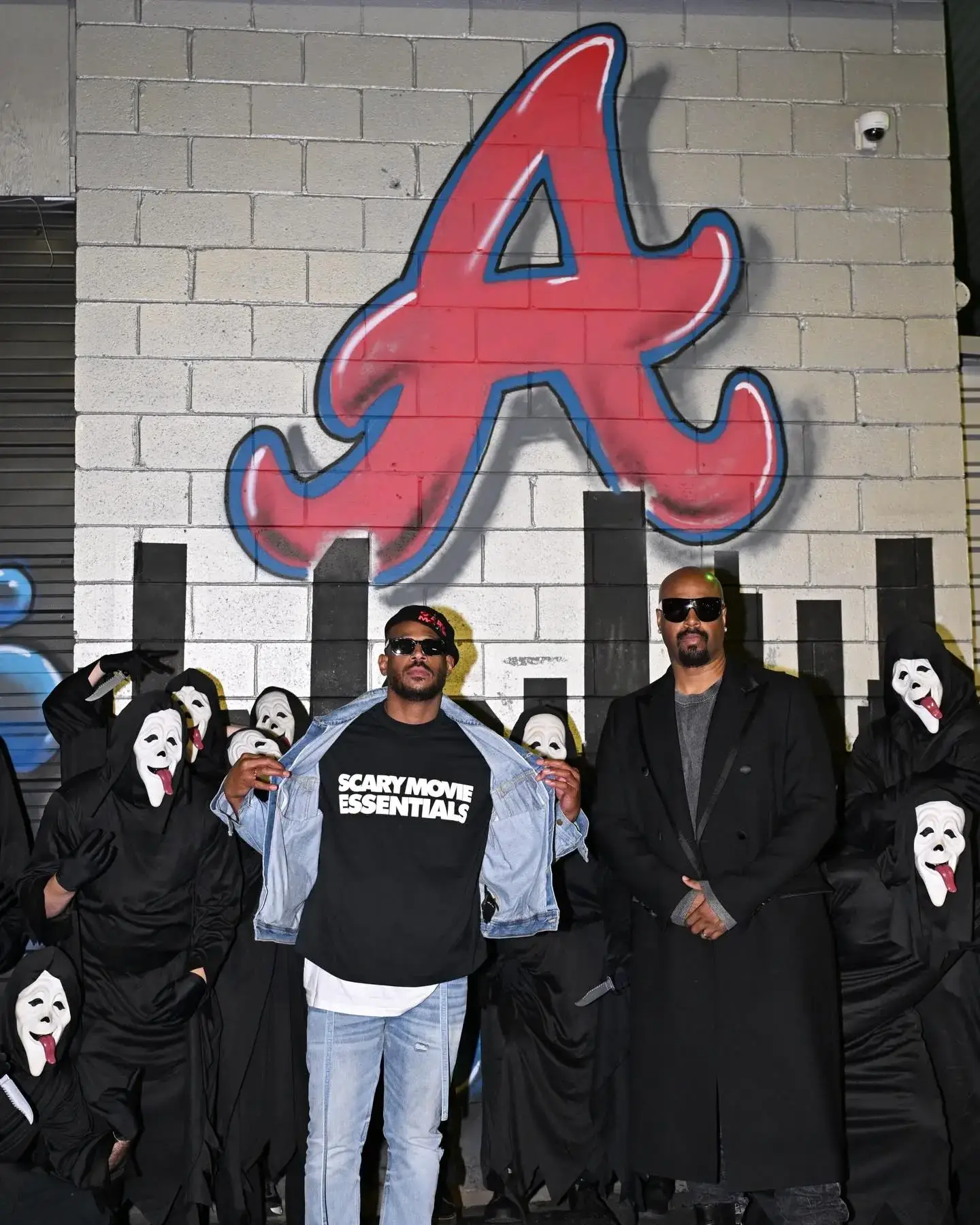 Marlon Wayans in a denim jacket and Shawn Wayans in a long black coat stand in front of a painted Atlanta Braves logo.