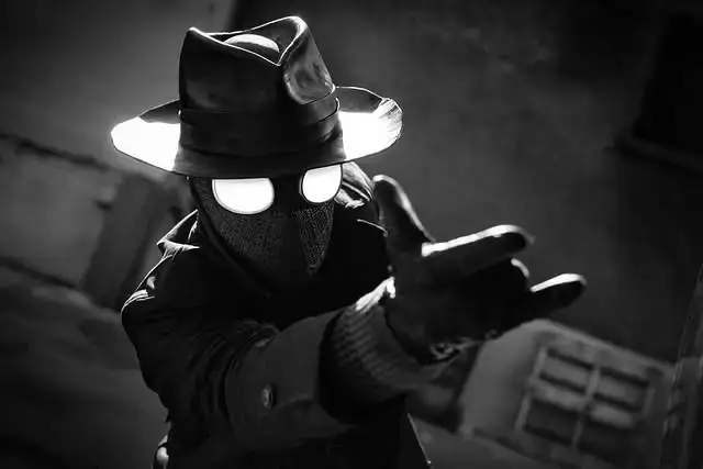 A black-and-white image of Spider-Man Noir wearing his signature fedora, mask with glowing white eyes, and a trench coat as he shoots web from his hand.
