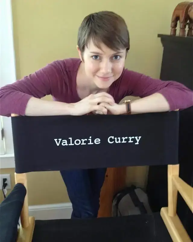 A young Valorie Curry with a pixie haircut smiles while leaning over the back of a black director