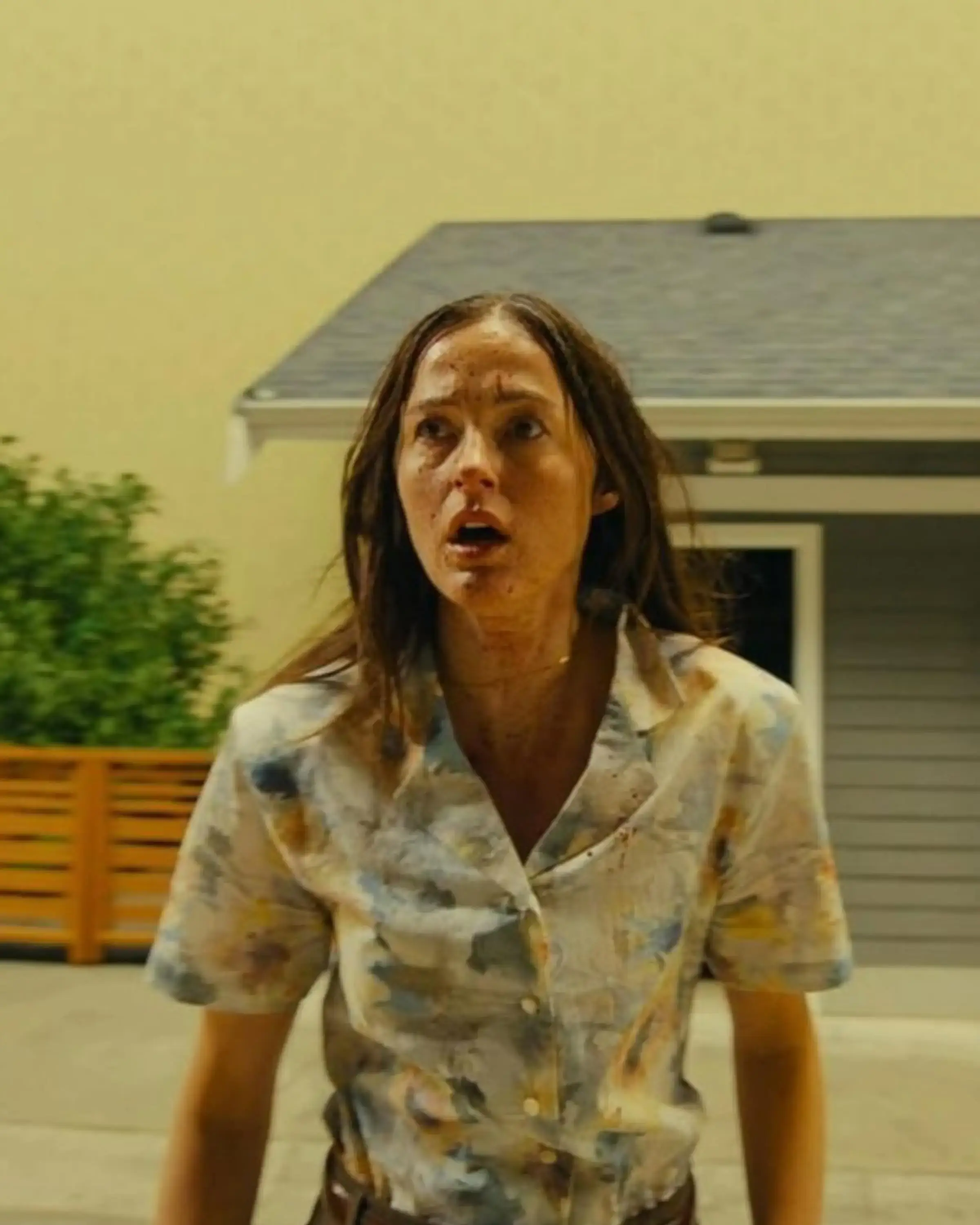 Renate Reinsve looks up in shock and horror while standing outside a suburban-style house inside a massive Backrooms environment.