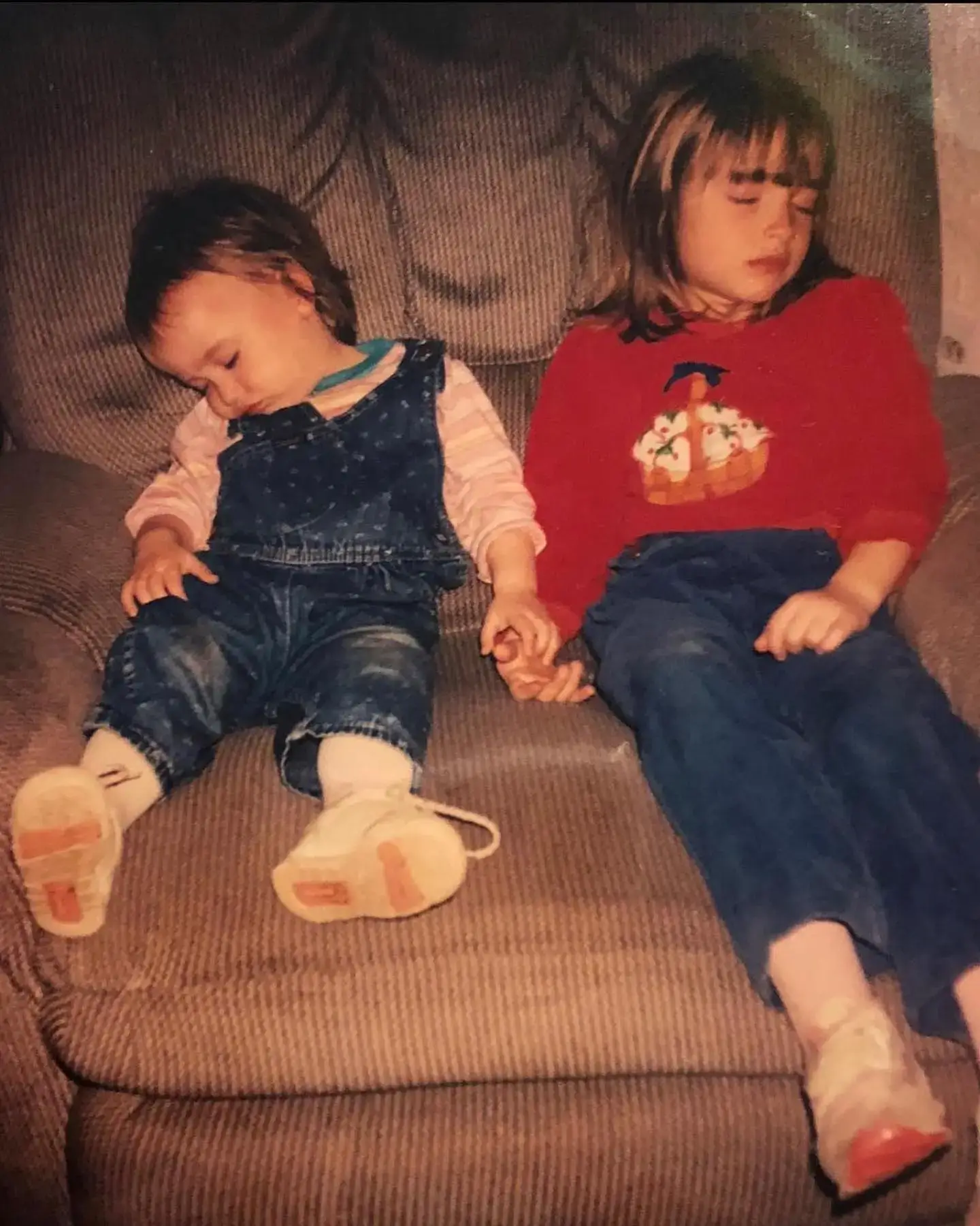 A young Alice Kremelberg and her sister Katina Kremelberg holding hands while fast asleep on an armchair.