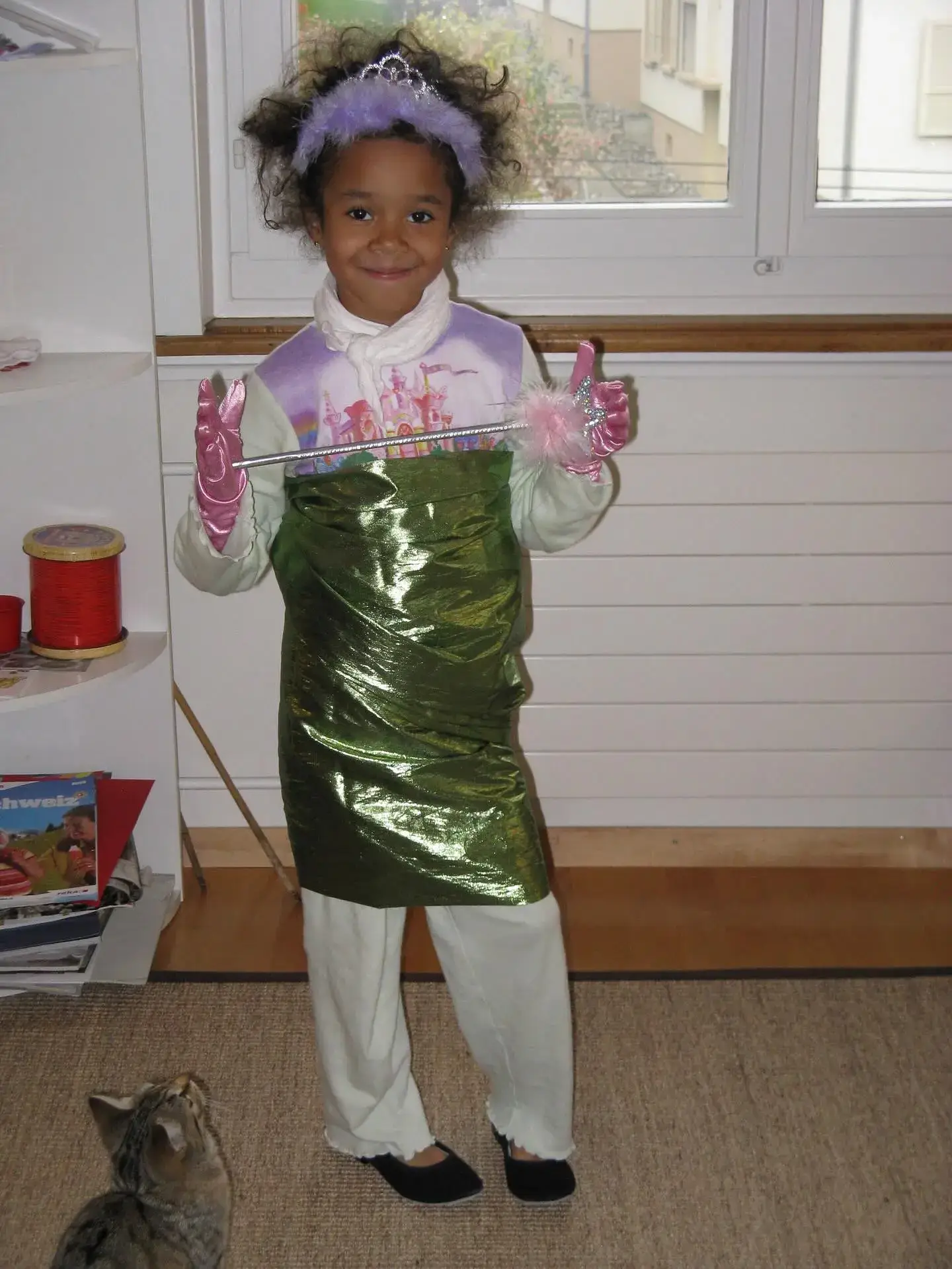 A young Manon Bannerman smiles while dressed up in a princess tiara, pink gloves, and a shiny green dress.