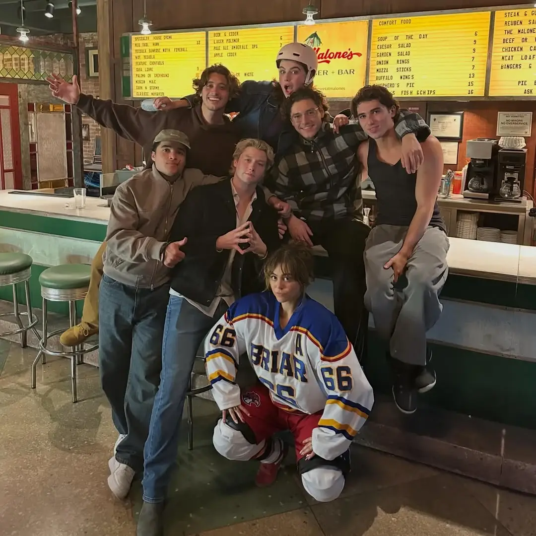 Mika Abdalla crouches in a white Briar hockey jersey in front of her Off Campus co-stars gathered around a bar counter.
