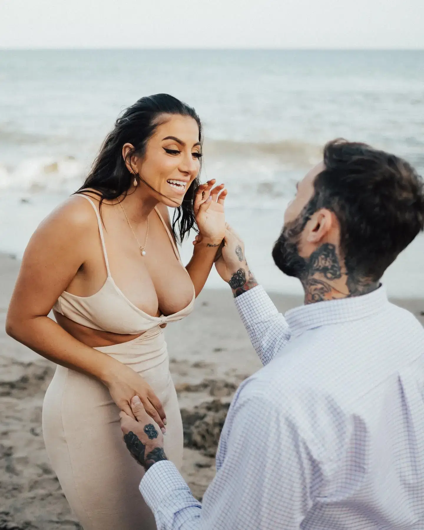 Adam22 holds hands with a smiling Lena the Plug on a sandy beach during an intimate proposal moment,