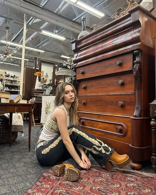 Daniela Avanzini  sits on a patterned rug next to a large antique wooden dresser inside a vintage store