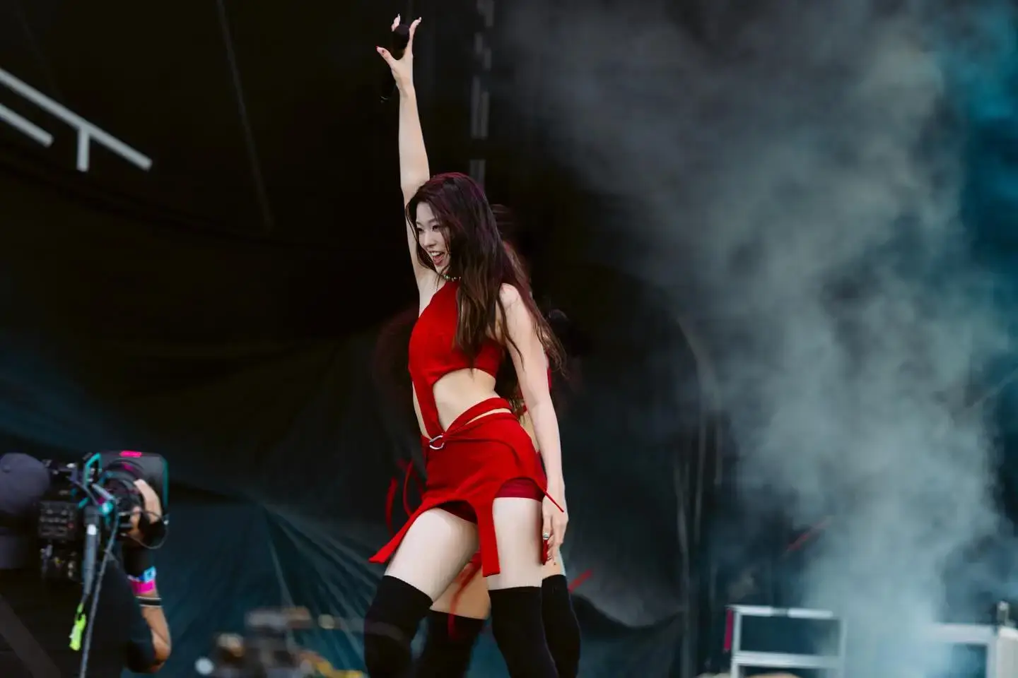 oonchae performs dynamically on stage in a red cutout outfit and thigh-high black socks, lifting her arm during a smoke-filled festival set.