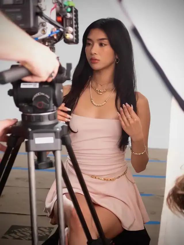 Sophia Laforteza sits in a light pink strapless dress and gold jewelry during a video shoot behind a camera setup.