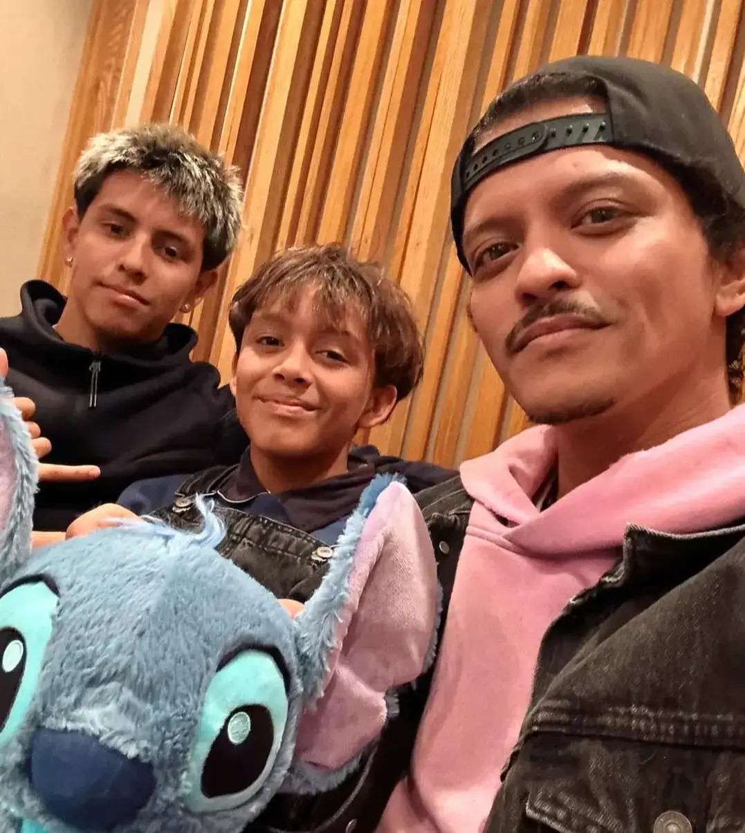 Bruno Mars in a backward cap and pink hoodie takes a selfie with his nephews Nyjah Music and Zyah Rhythm, who holds a blue Stitch plush toy.