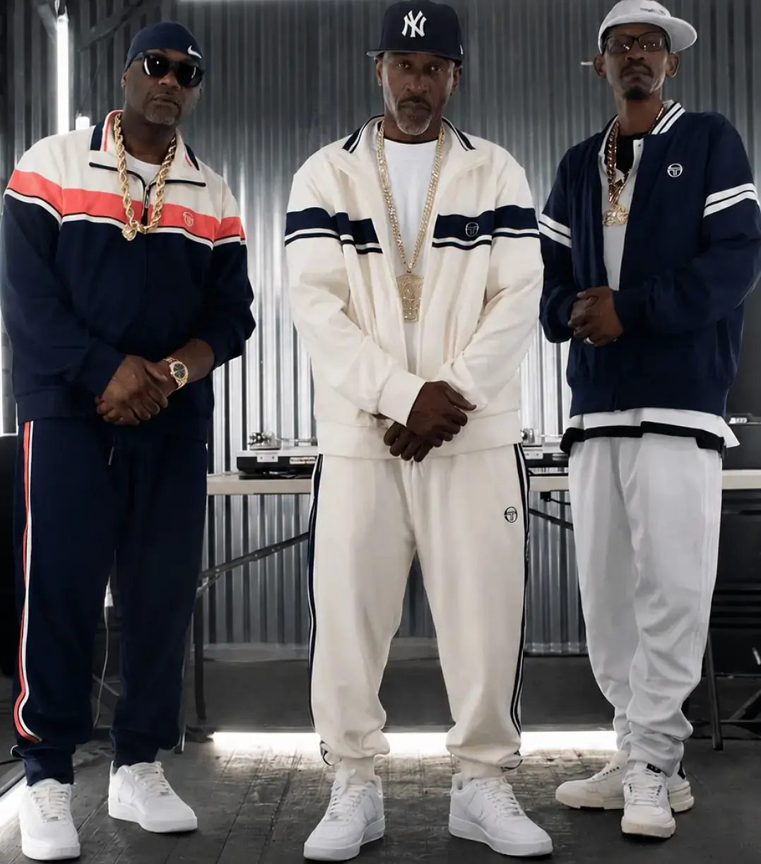 Hip-hop pioneers Eric B., Rakim, and K-Solo pose together in matching Sergio Tacchini tracksuits, white sneakers, and heavy gold chains.
