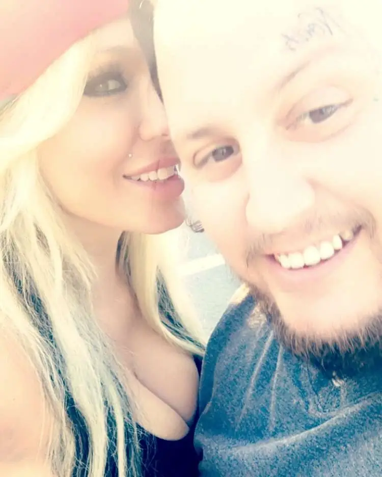 A close-up, overexposed selfie of Jelly Roll smiling broadly alongside his wife Bunnie XO, who smiles from behind his shoulder.