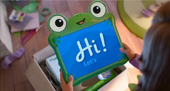 A child holds a green, frog-shaped "Lilypad" smart tablet displaying a blue screen that says "Hi! Let