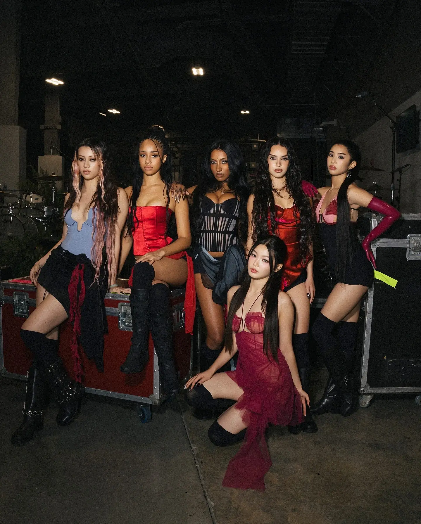 The six members of global girl group KATSEYE where Megan, Manon, Lara, Yoonchae, Daniela, and Sophia, pose confidently in stylish red, black, and blue outfits backstage.