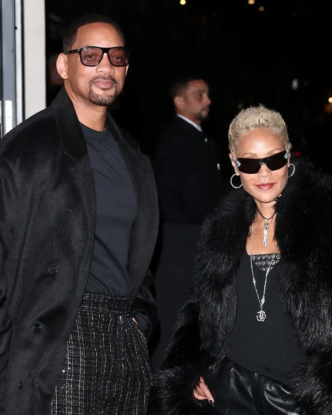 Will Smith and Jada Pinkett Smith pose together at night wearing stylish black coats and sunglasses