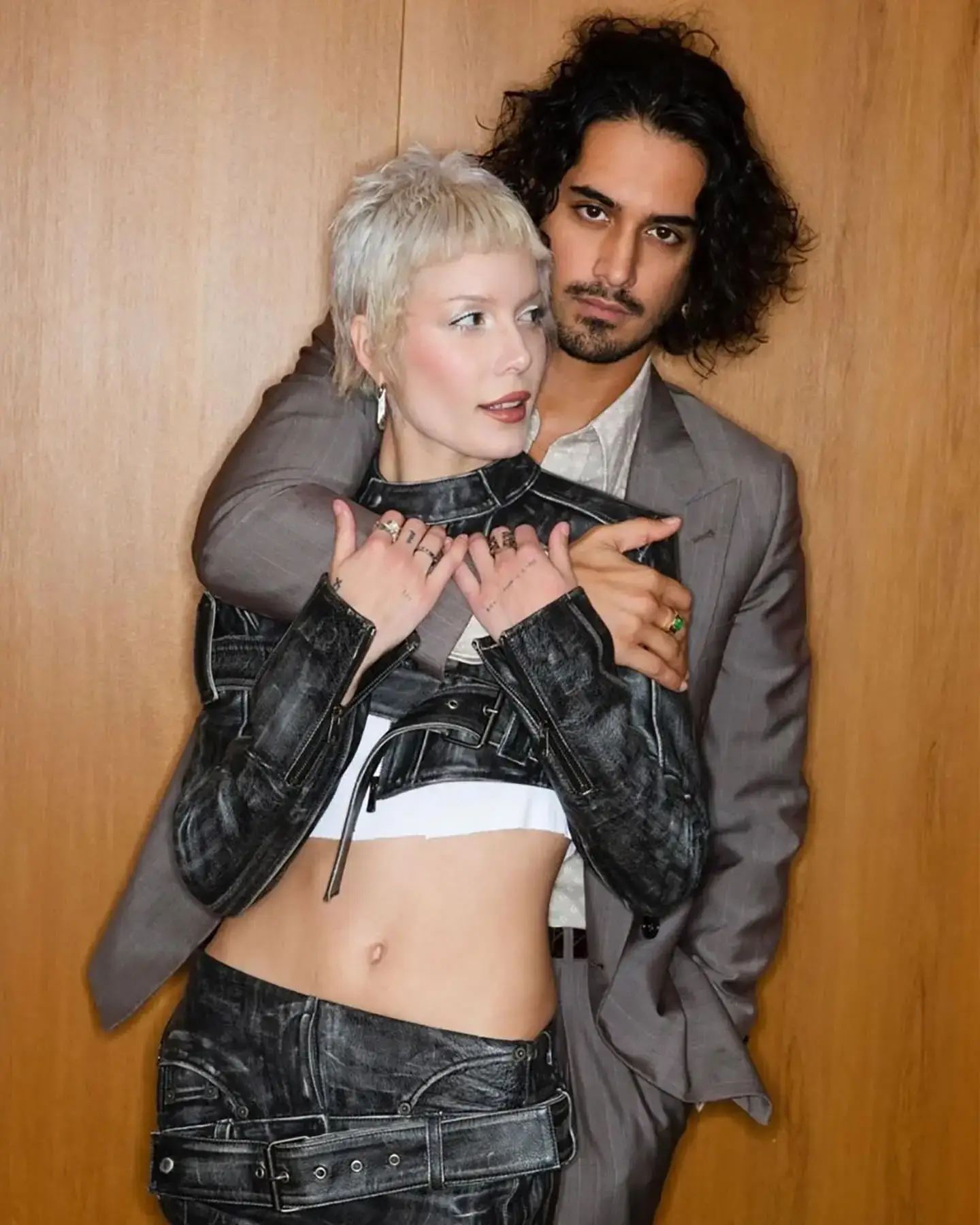 Avan Jogia stands behind his girlfriend Halsey, holding her affectionately as they pose together against a wooden wall.