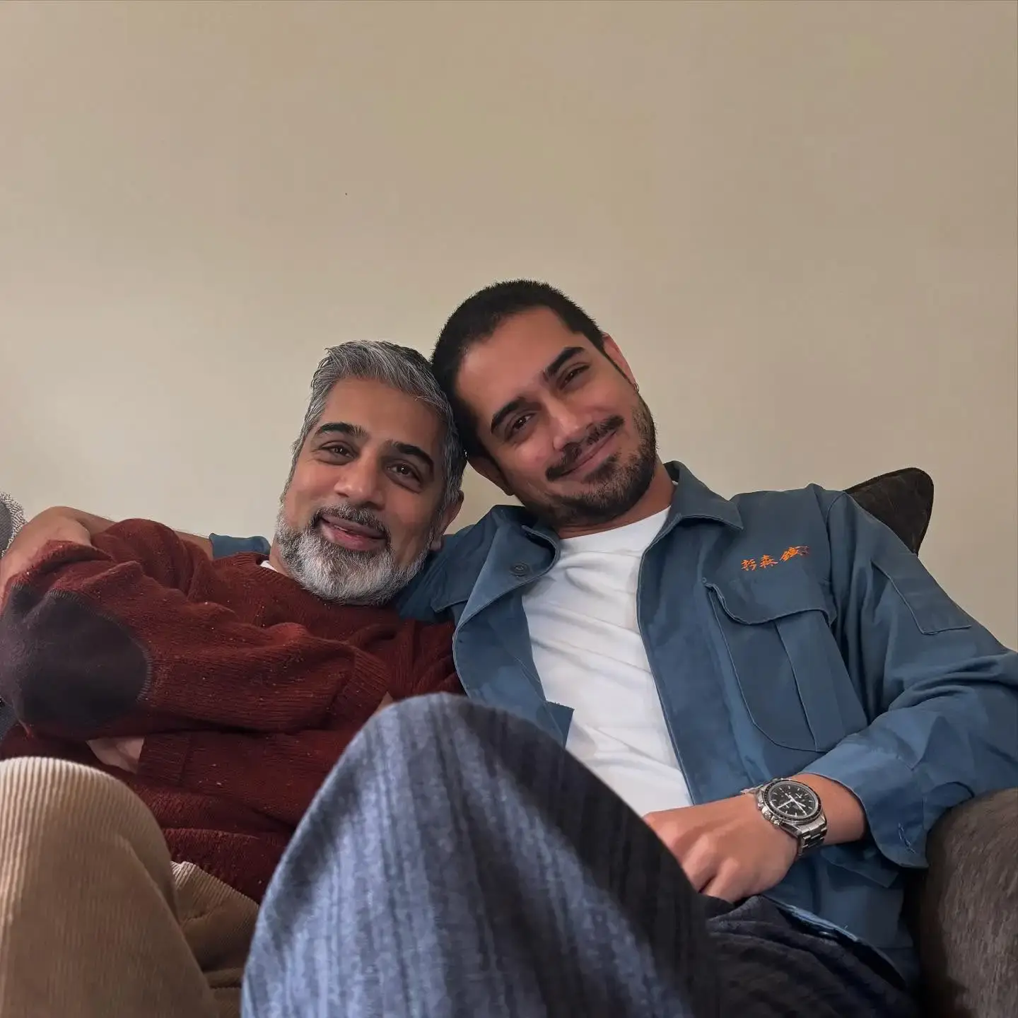 Avan Jogia smiles and leans his head against his dad, Mike Jogia, as they sit comfortably together on a couch.