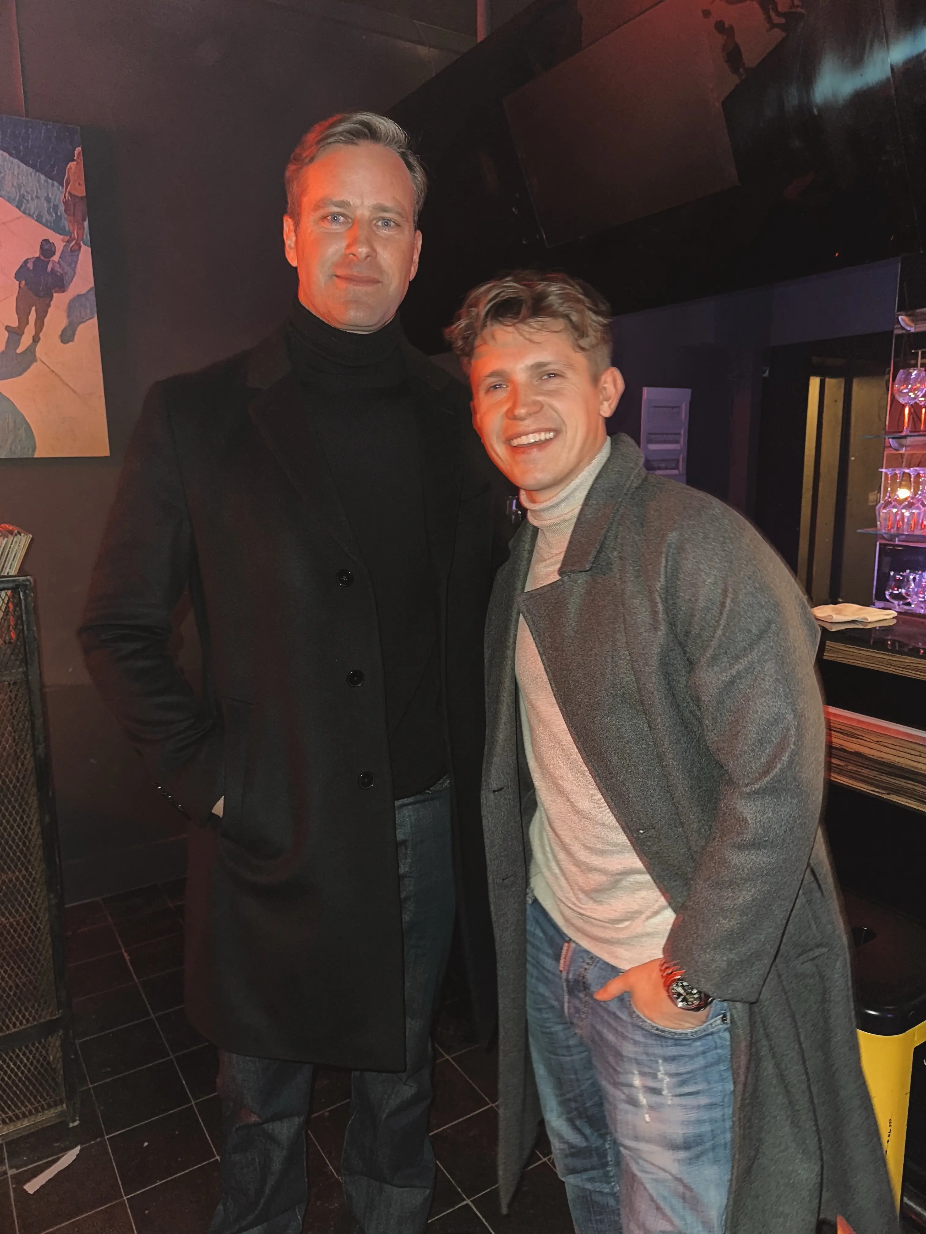 German actor Lennart Betzgen smiles broadly next to American actor Armie Hammer inside a dimly lit venue.